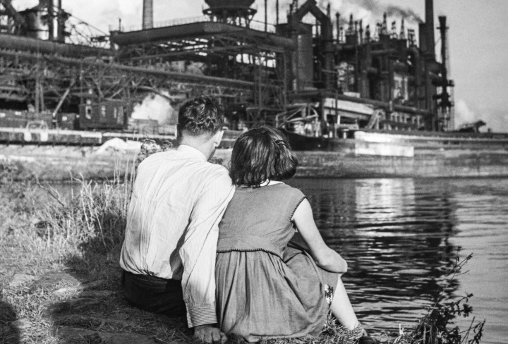 Historisches Schwarzweiß-Foto eines Pärchens, das auf Industrieanlage an einem Fluss schaut
