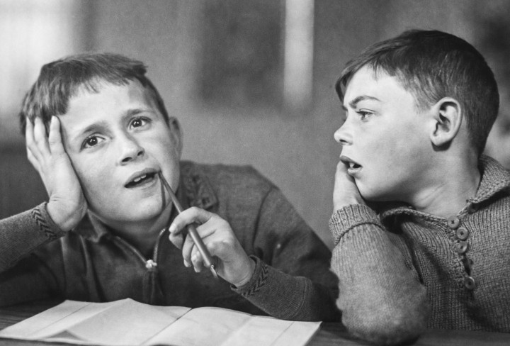 Zwei Jungen sitzen grübelnd über einem Schulheft