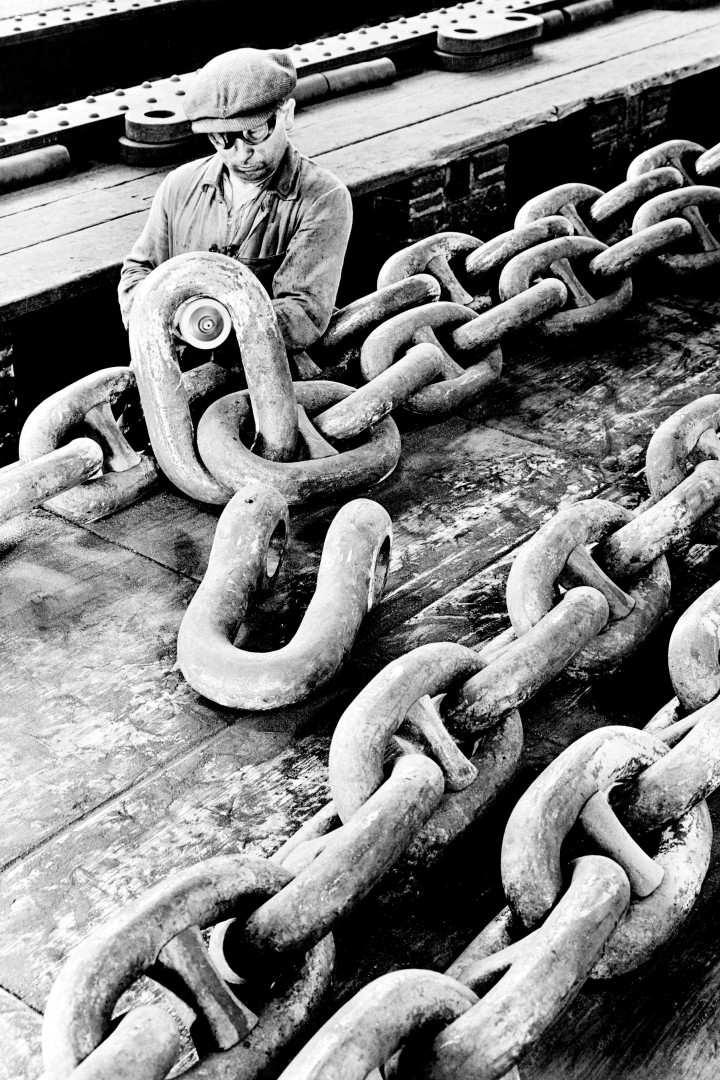 Historisches Schwarz-weiß-Foto eines Fabrikarbeiters an einer dicken Stahlkette