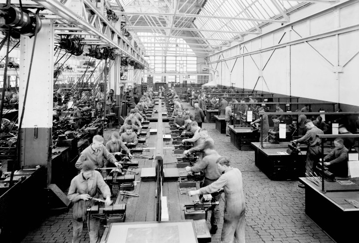 Schwarzweiß-Bild einer großen Fabrikhalle mit zahlreichen Arbeitern an Werkbänken