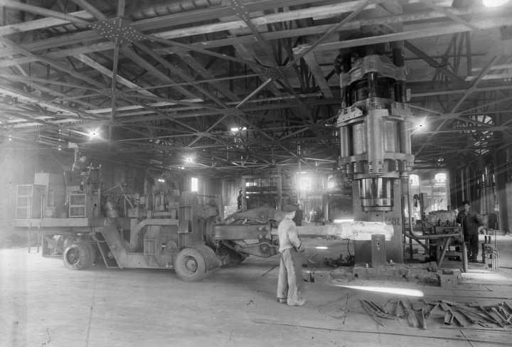 Schwarzweiß-Bild aus einem Stahlwerk mit Arbeitern und großen Maschinen