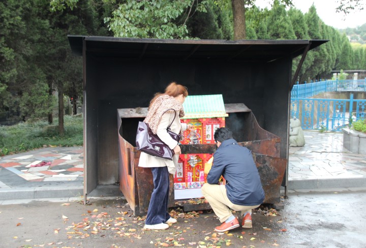 Mann und Frau verbrennen eine Opfergabe auf einem Friedhof
