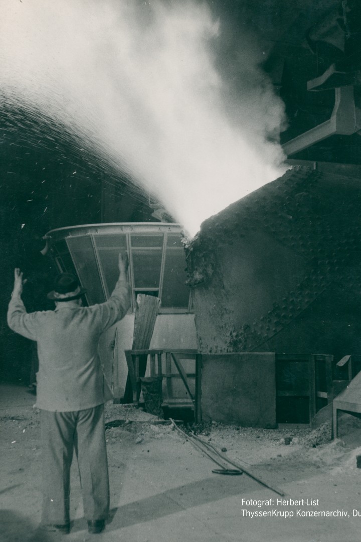 Schwarz-weiß-Foto von sprühenden Funken und einem Mann, der vor der Maschine Anweisungen gibt