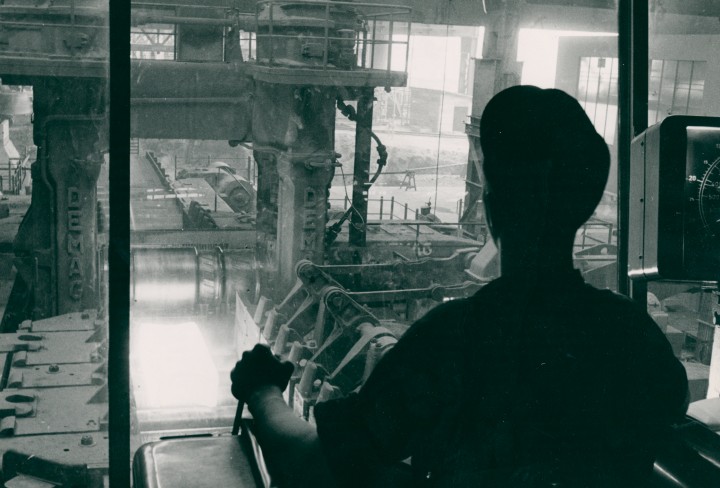 Schwarz-weiß-Foto eines Mannes, der eine Maschine in einem Stahlwerk steuert