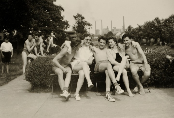 Historisches Schwarz-Weiß Foto von einer Gruppe Jugendlicher im Freibad Elpenbach mit der Zeche Jacobi im Hintergrund