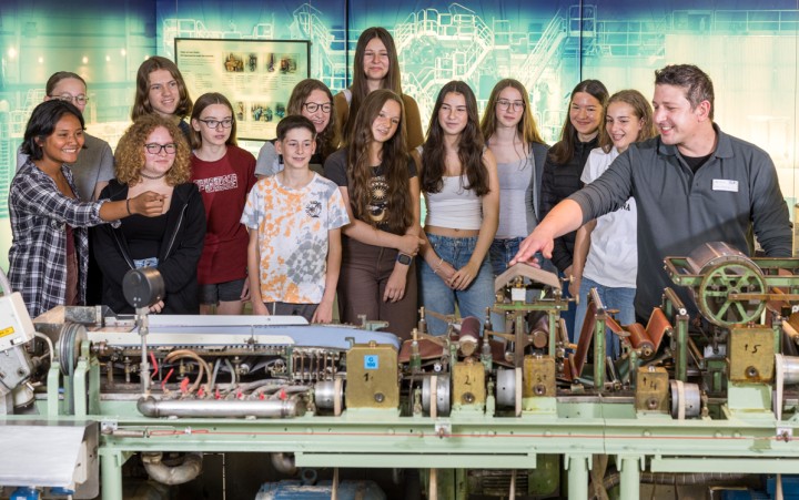 Mädchen und Jungen mit Museumsmitarbeiter an einer großen Papiermaschine