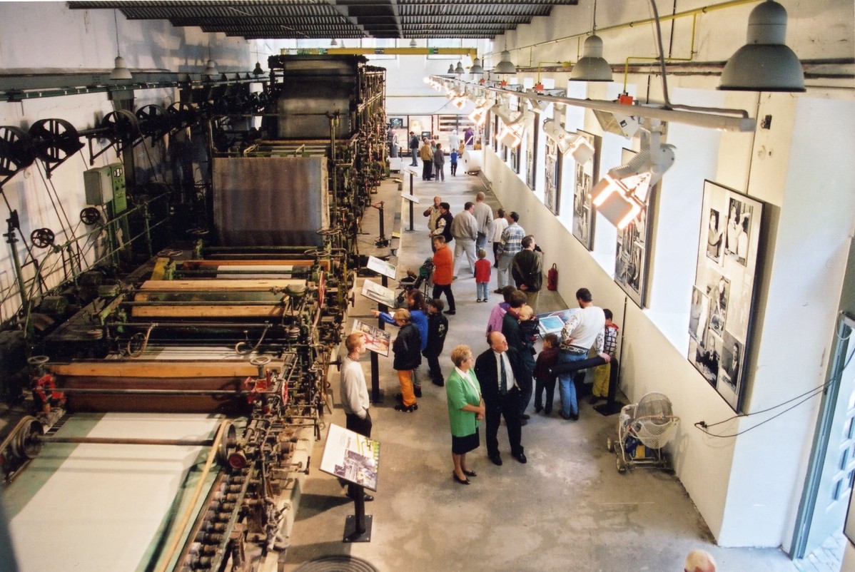 Papiermaschinenhalle mit riesiger Papiermaschine, daneben Besucherinnen und Besucher