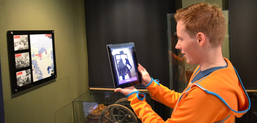 Junger Mann steht mit einem Tablet-Computer in der Ausstellung der St. Antony-Hütte