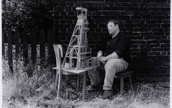 Schwarz-weiß-Fotografie eines Mannes, der ein Förderturm-Modell betrachtet